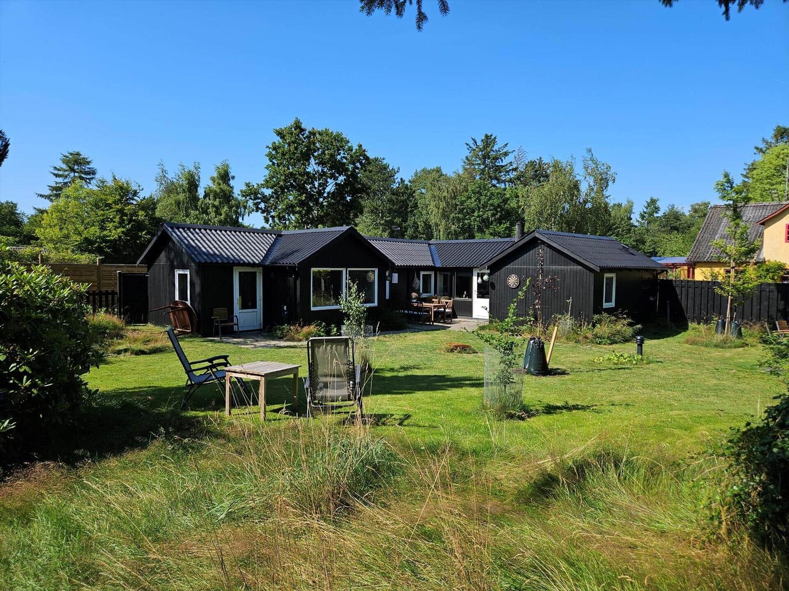 Black wooden cabin with garden and seating areas under blue sky.