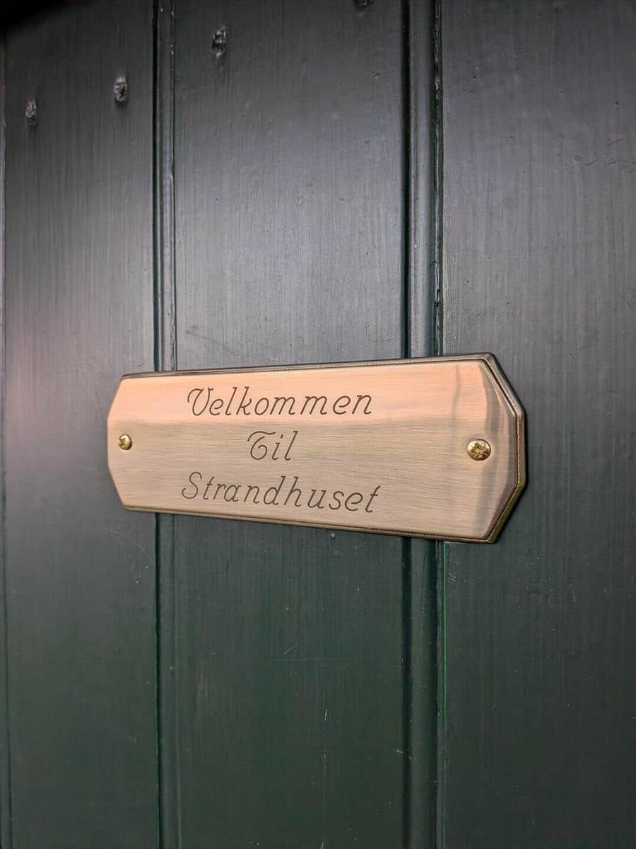 Holztafel mit Aufschrift: Velkommen Til Strandhuset an einer grünen Tür.