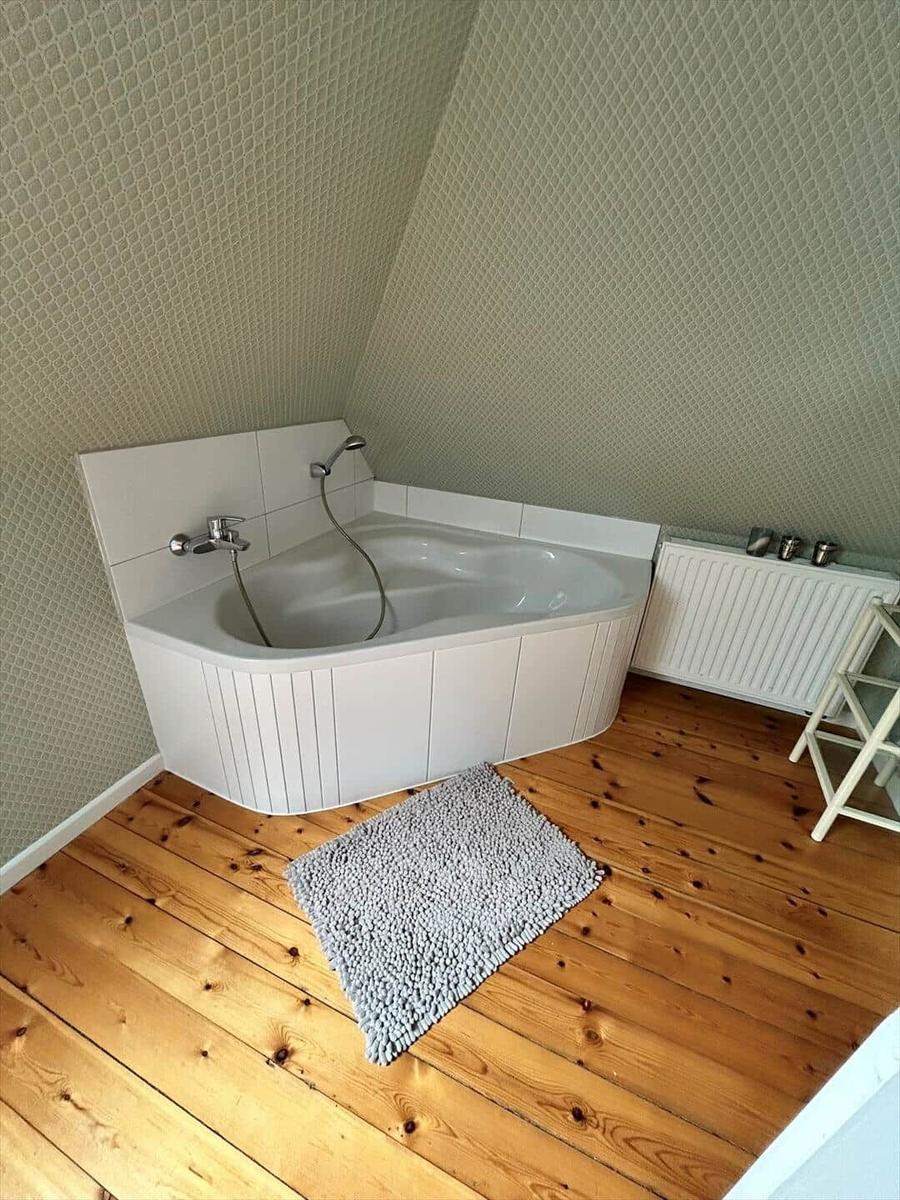 Bath with corner bathtub, wooden floor, and patterned wall cladding.