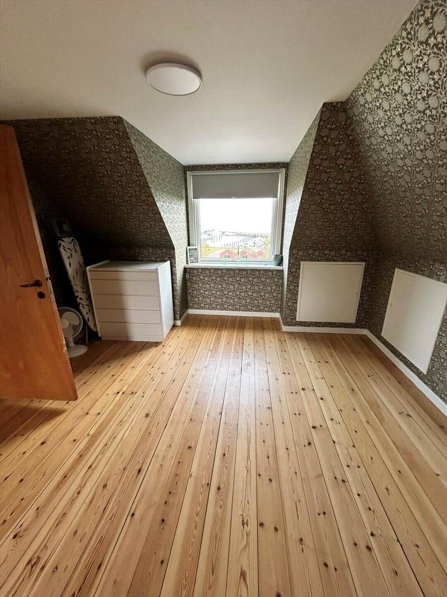 Room with wooden floor, patterned wallpaper, and window with view.