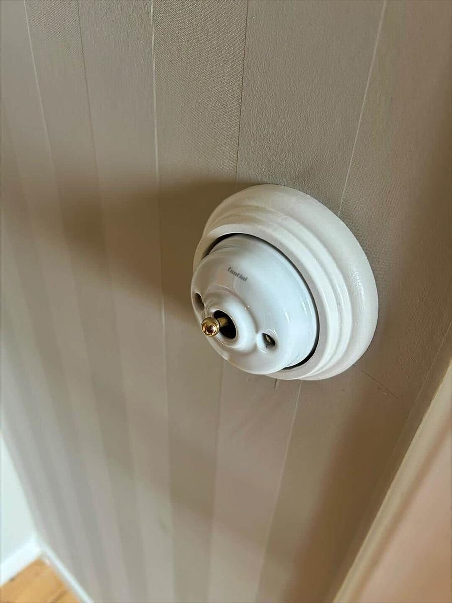 White ceiling light fixture with gold screw head on vertically striped wall.