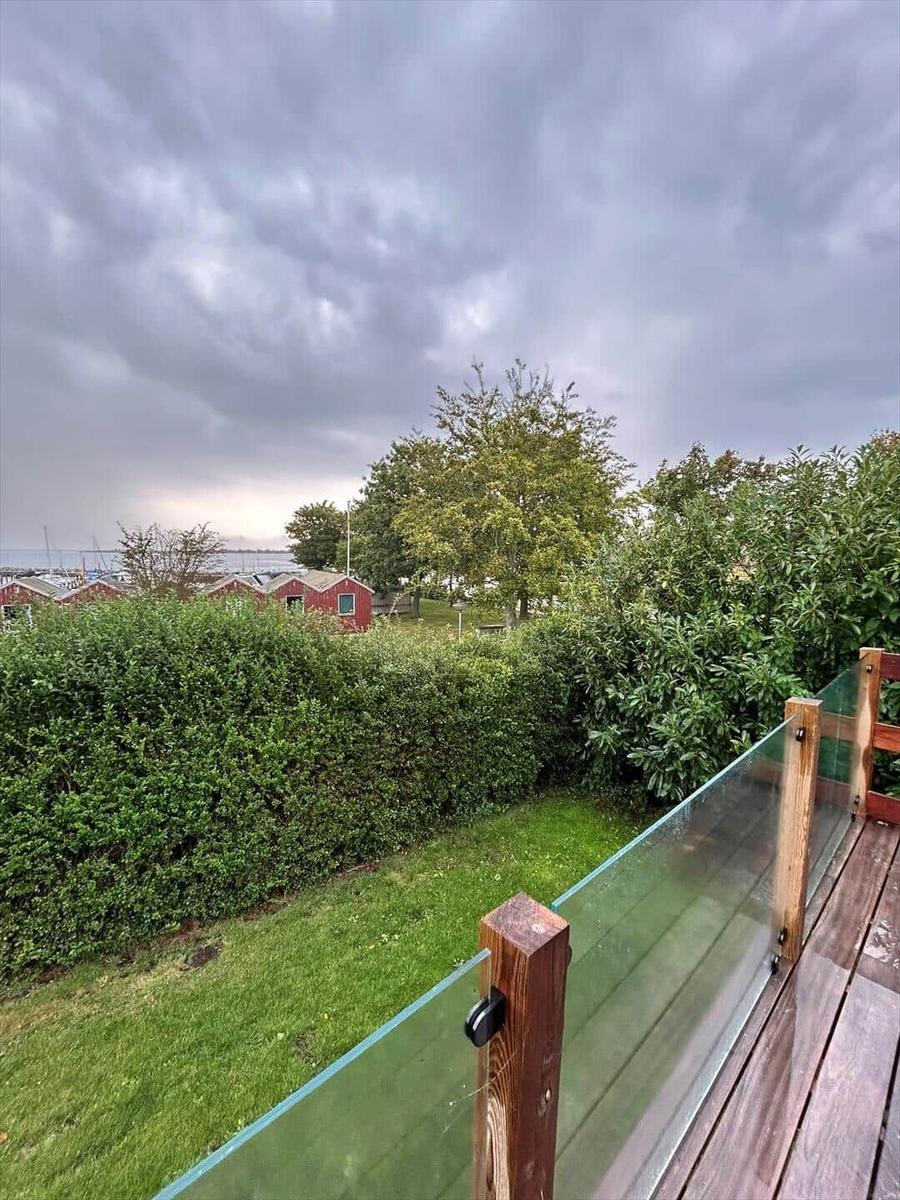 Deck with glass railing overlooking green areas and red houses.
