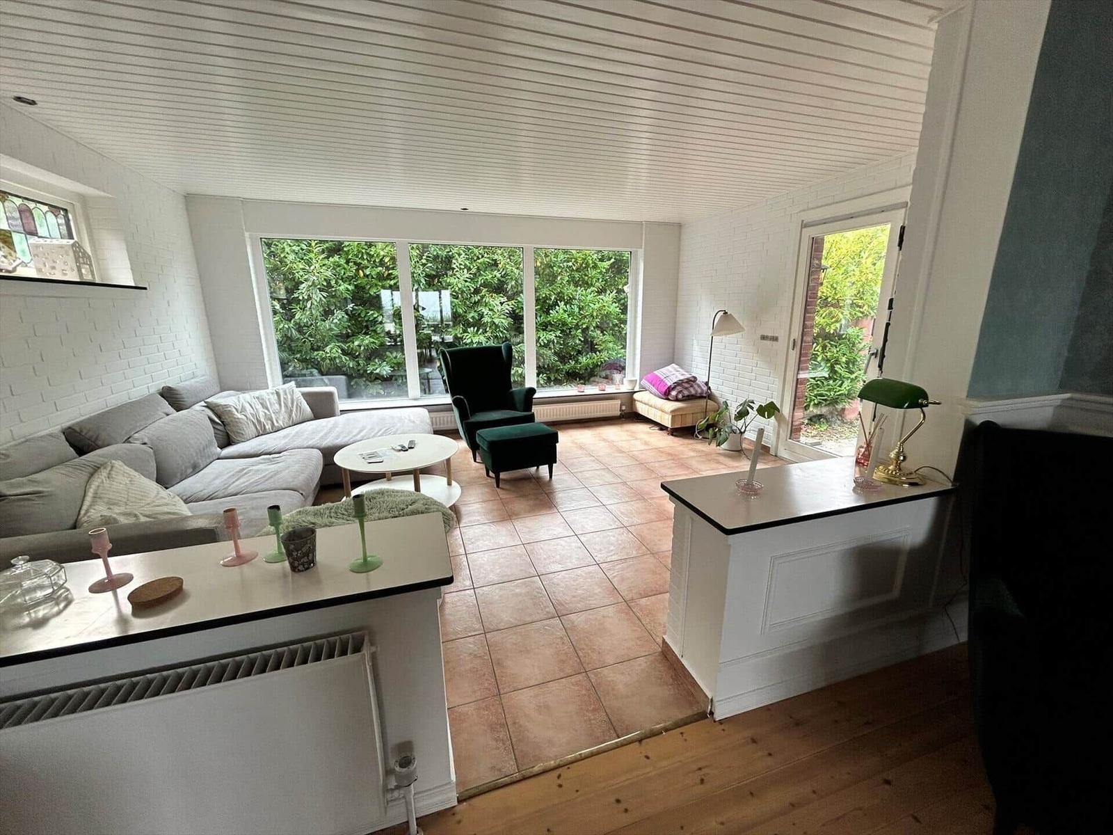 Living area with sofa, armchair, and large window overlooking green outdoor space.