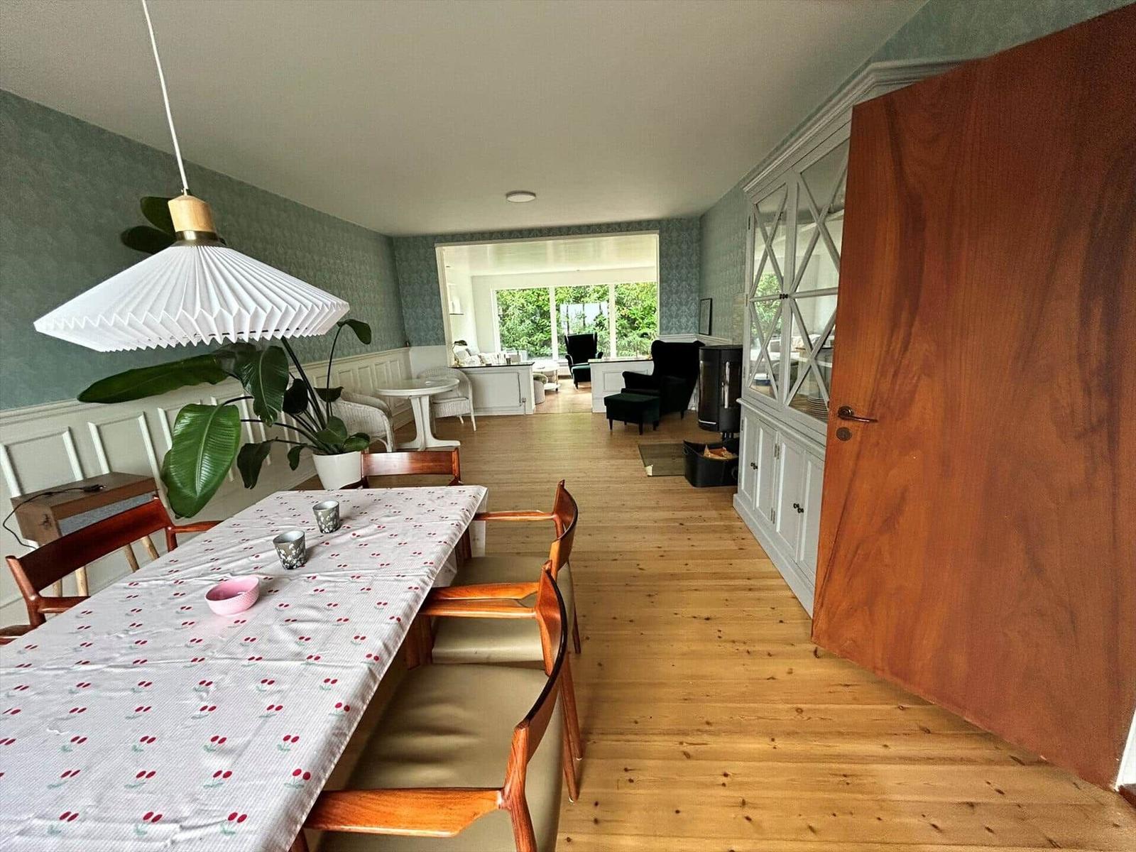 Dining area with table, chairs, and plant. Wooden floor and white furniture are visible.