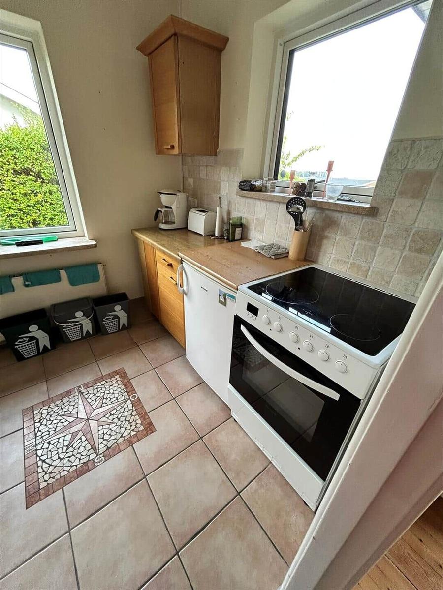 Kitchen with stove, fridge, and windows. Tile floor and mosaic mat.
