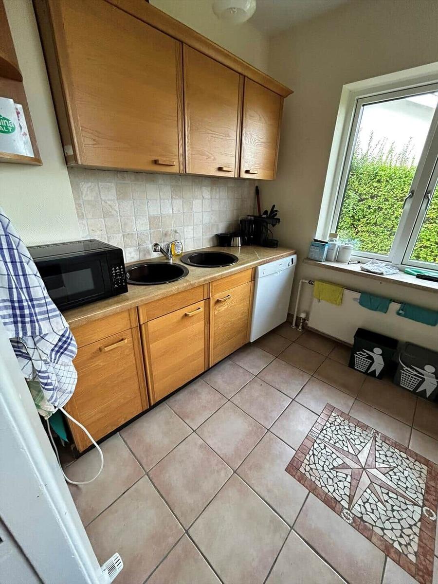 Kitchen with wooden cabinets, two sinks, microwave, and window overlooking greenery.