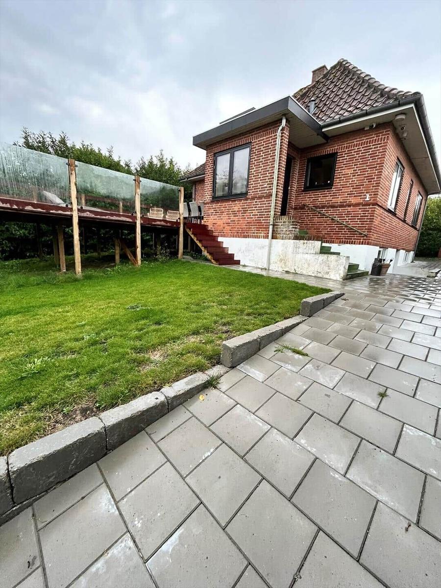 Red brick house with terrace and lawn. Paved path leads to the entrance.