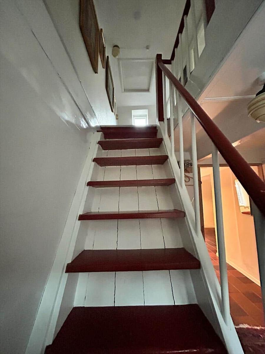 Staircase with red steps and white walls. Handrail and ceiling are visible.
