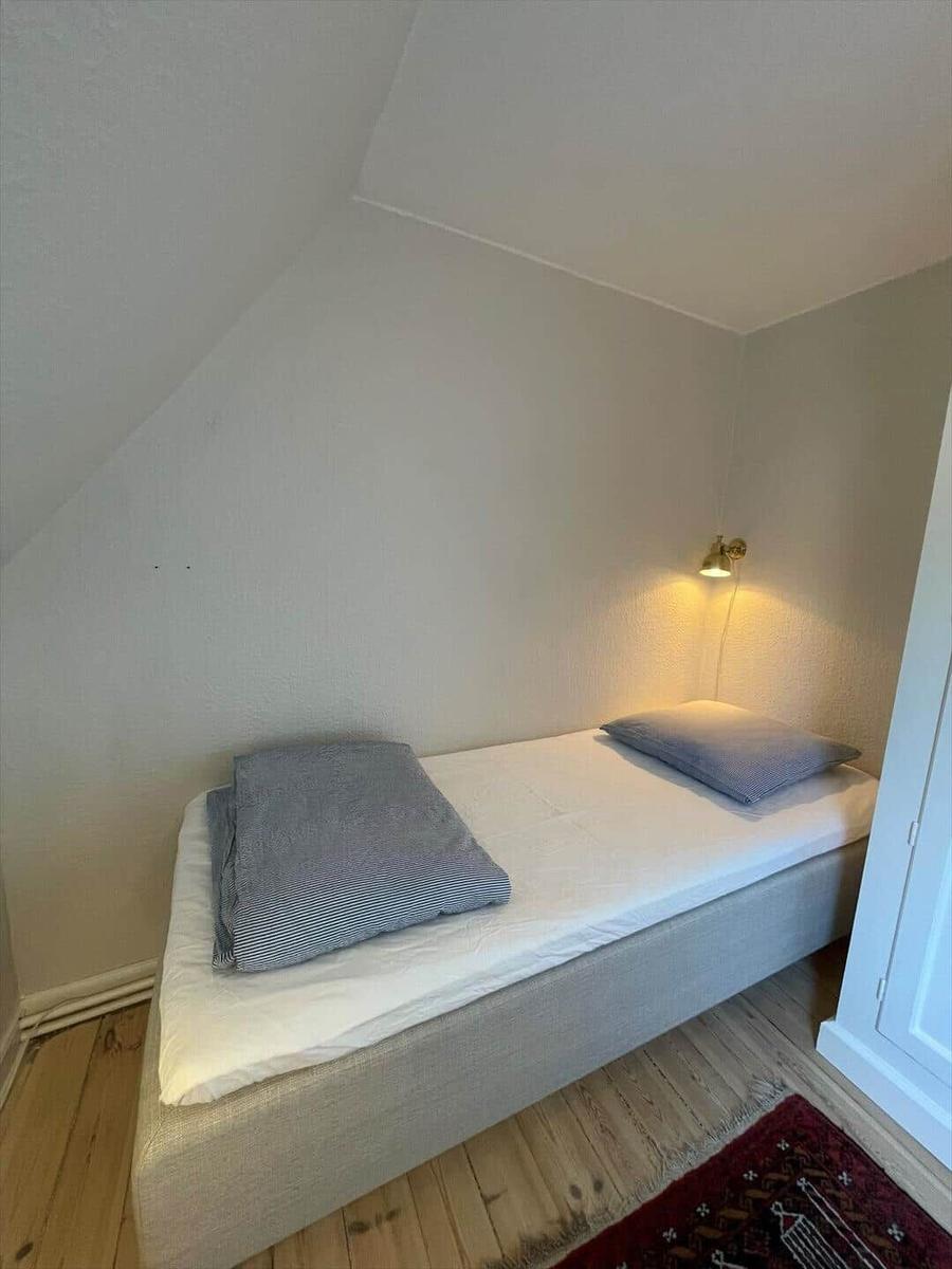 A bedroom with sloped ceiling, bed, wall lamp, and wooden floor.