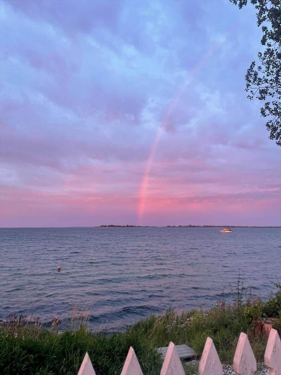 A rainbow in the sky over the sea, a small boat is visible in the background.