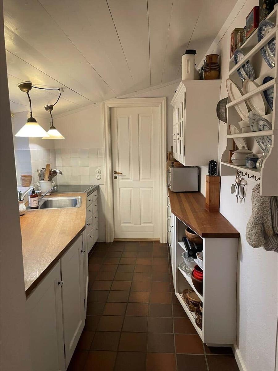Kitchen with white cabinets, wooden countertop, and tiled floor. Dishware and kitchen utensils are visible.