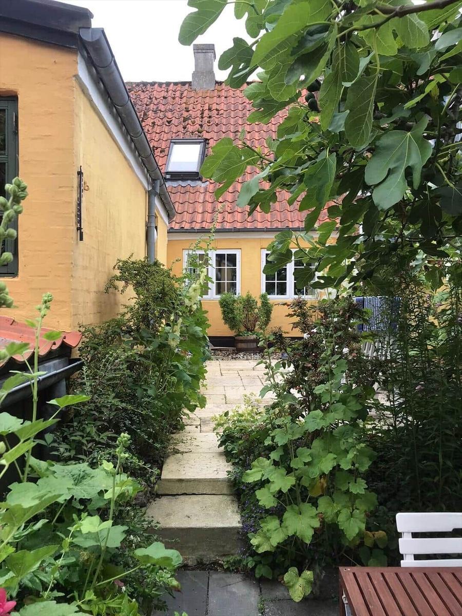 Stone path leads to a yellow house with red roof and windows.