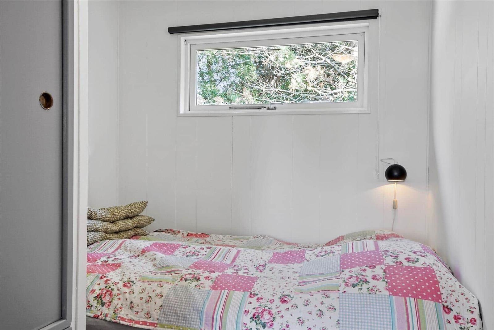Schlafzimmer mit Bett, Fenster und Wandlampe. Decke mit Patchwork-Muster.