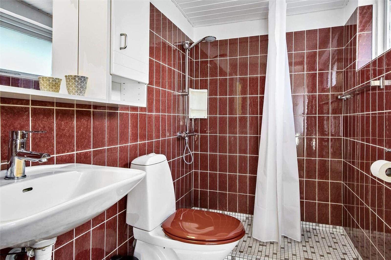 Badezimmer mit Dusche, Toilette und Waschbecken. Wandfliesen in Rottönen.