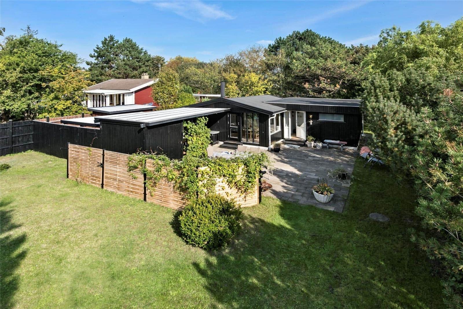 Schwarzes Haus mit Terrasse und Garten. Umgeben von Bäumen und Gras.