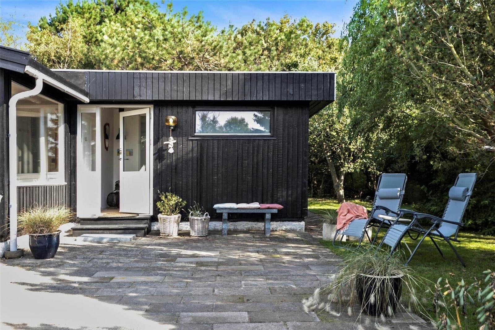 Schwarzes Holzhaus mit Terrasse, Sitzbank und Liegestühlen im Garten.