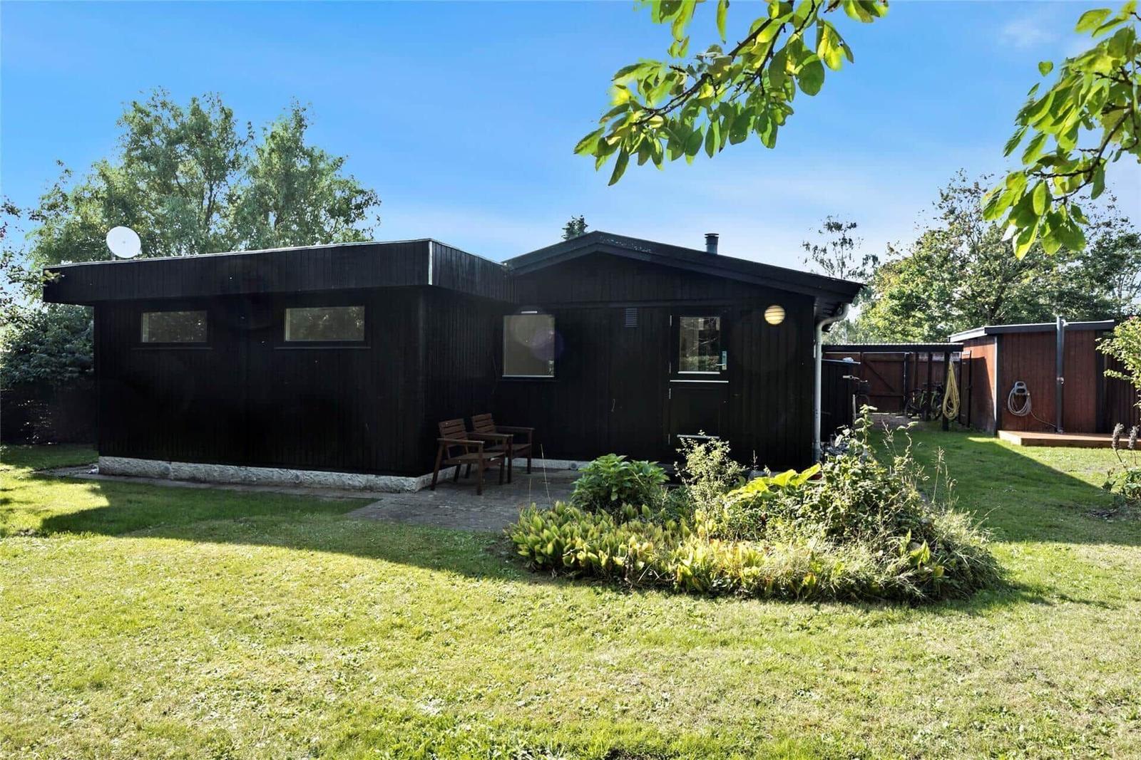 Schwarzes Holzhaus mit Garten, Sitzgelegenheit und Satellitenschüssel.