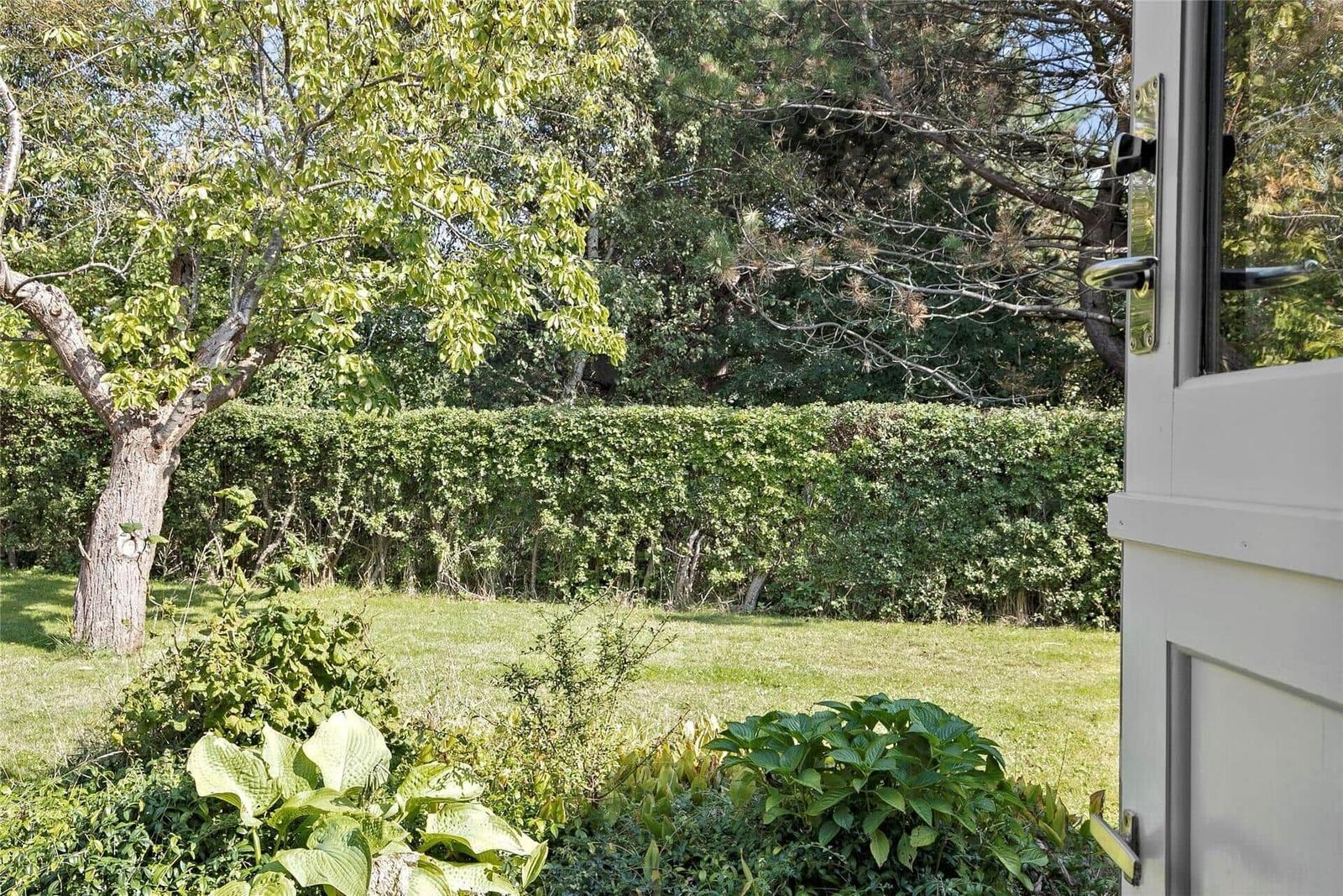 Durch die Tür blickt man auf einen grünen Rasen mit Hecke und Bäumen.