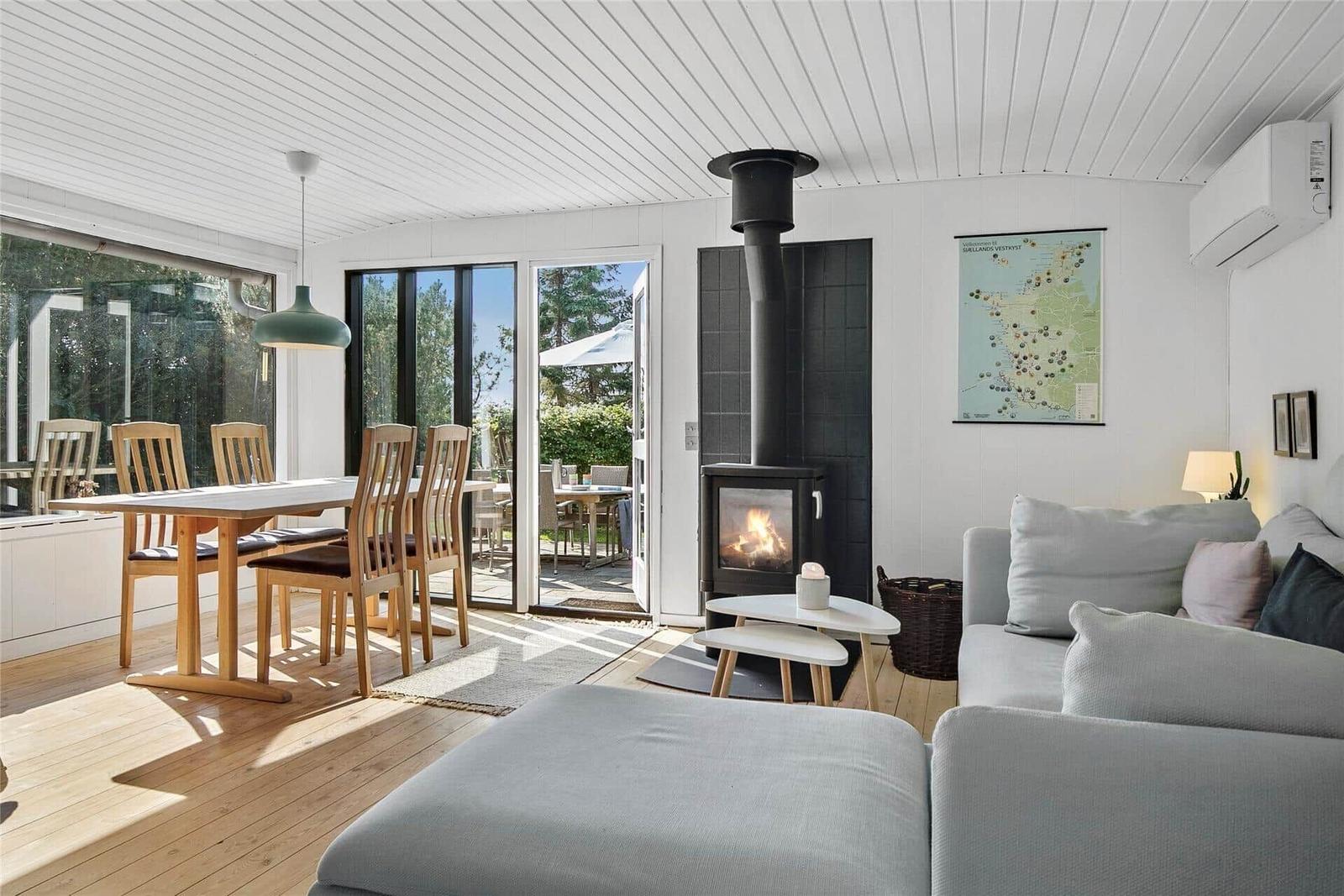 Wohn- und Essbereich mit Kamin, Sofa und Terrassentür. Holzboden und große Fenster.