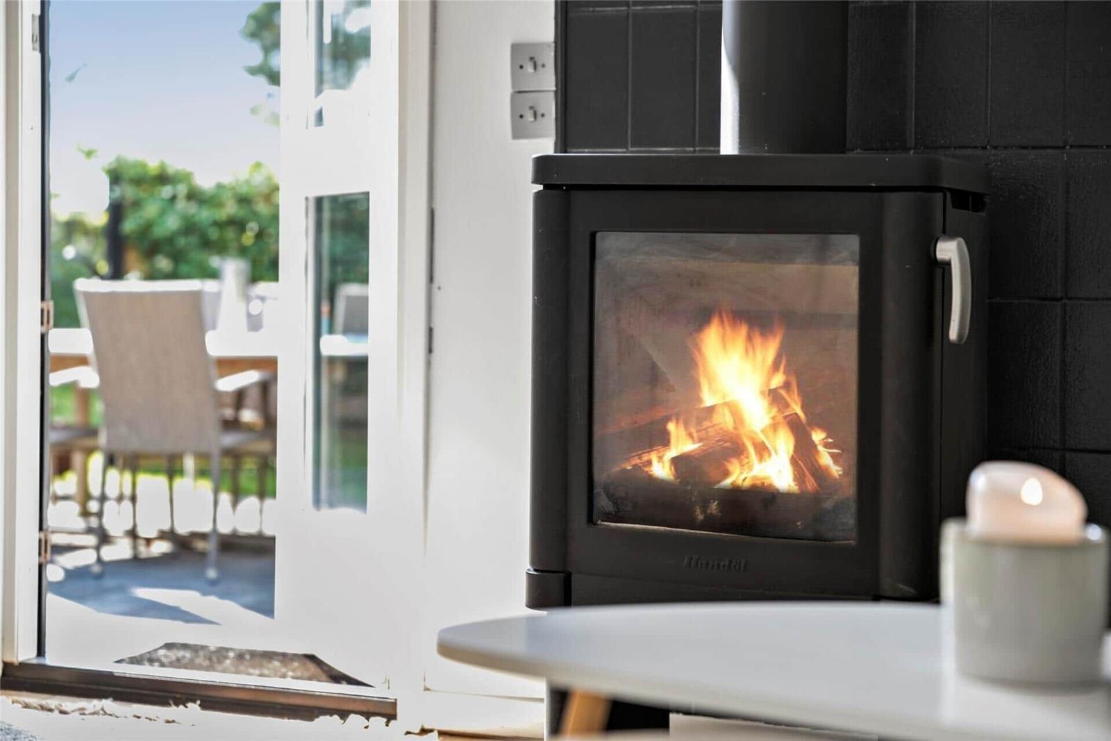 Ein Kaminofen mit brennendem Holz steht vor einer Glastür zum Garten.