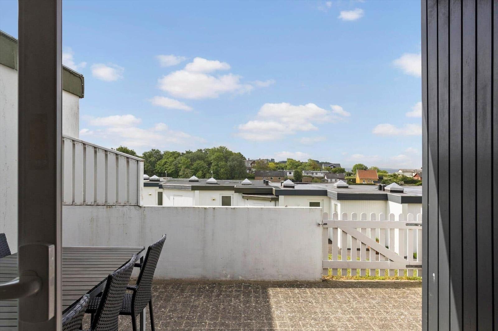 Terrasse mit Tisch und Stühlen, Blick auf Dächer und Bäume unter blauem Himmel.