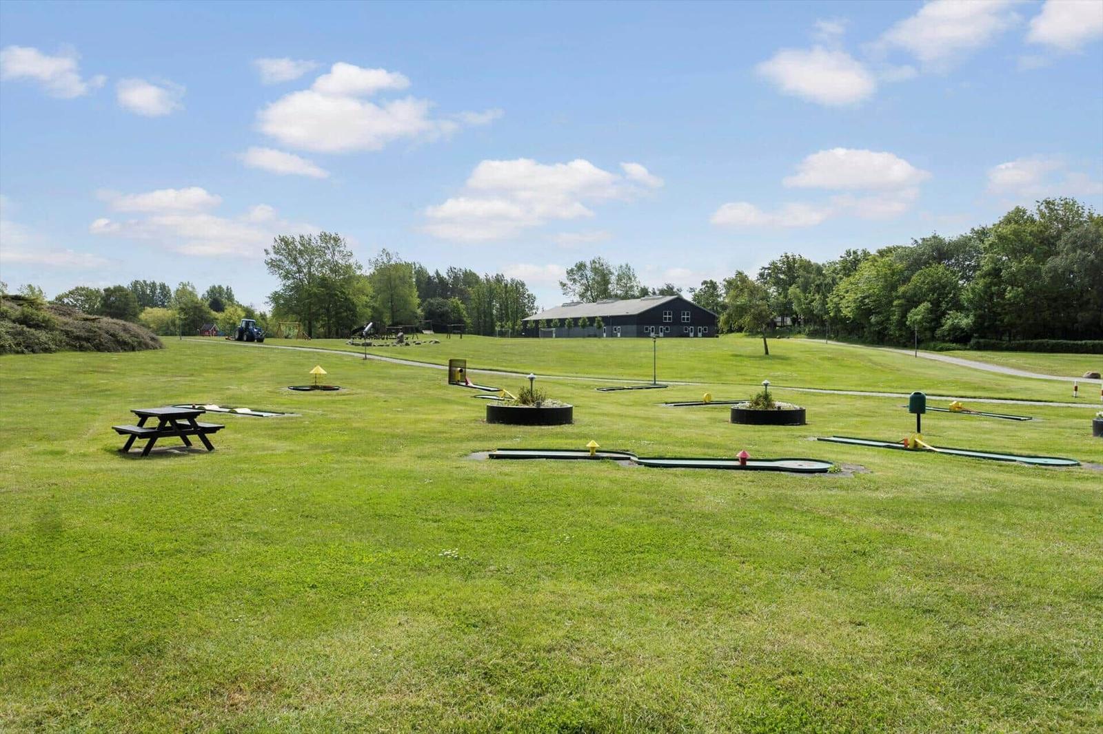 Grünes Feld mit Minigolf, Picknicktisch und Spielplatz. Im Hintergrund ein dunkles Gebäude.