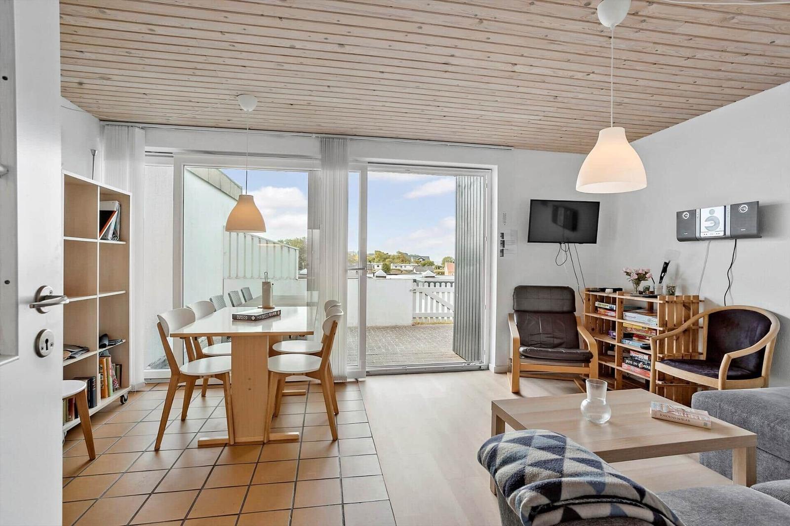Wohn- und Essbereich mit Blick auf Balkon. Holzdecke, TV und Sitzgelegenheiten.