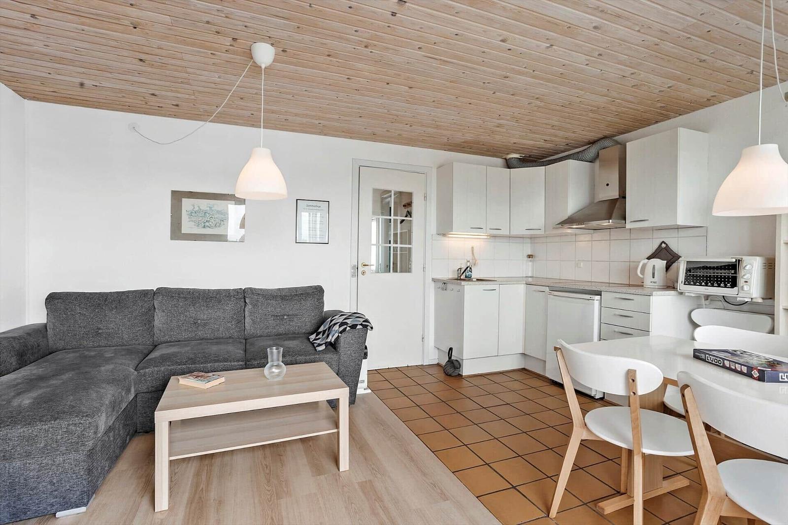 Wohnbereich mit Sofa, Esstisch und Küche unter Holzdecke.