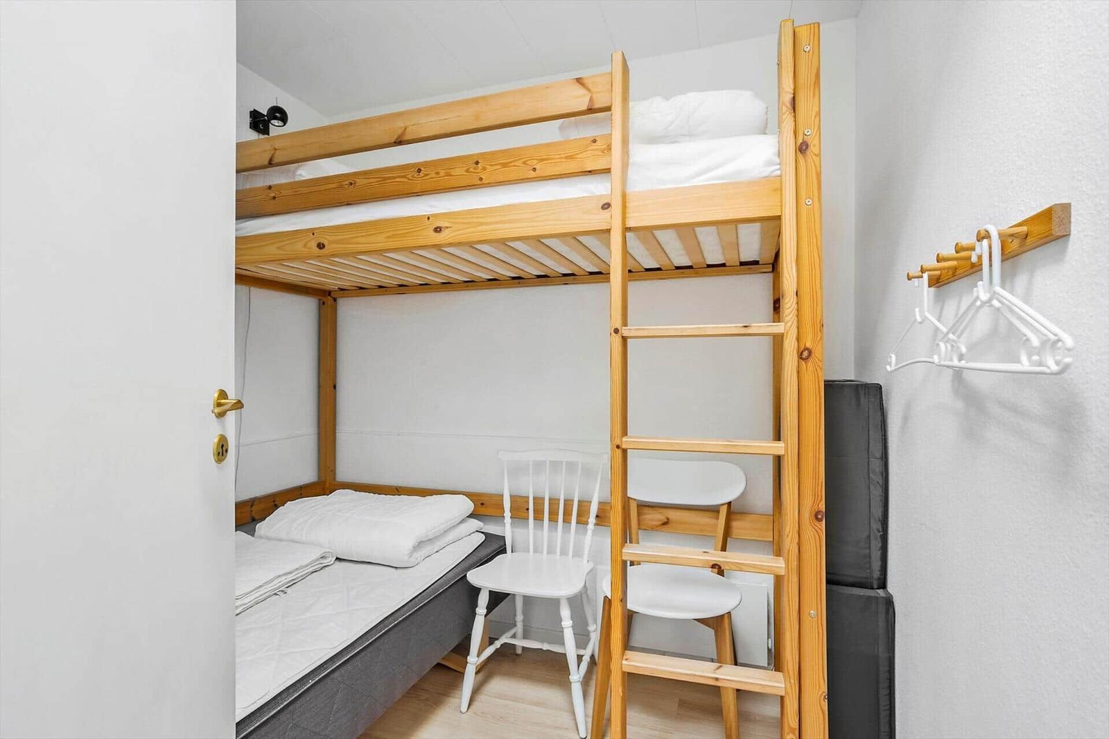 Zimmer mit Holz-Kojenbett, Stuhl und Kleiderhaken an der Wand.