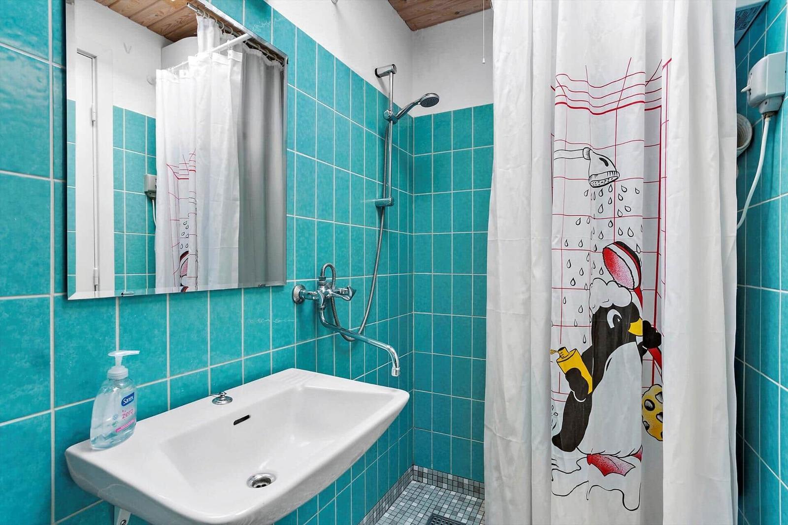 Badezimmer mit Dusche, Waschbecken und Spiegel. Wandfliesen sind türkisfarben.