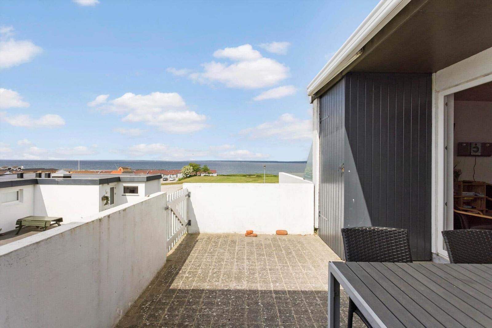 Terrasse mit Tisch und Stühlen, Blick auf Meer und Grünflächen.