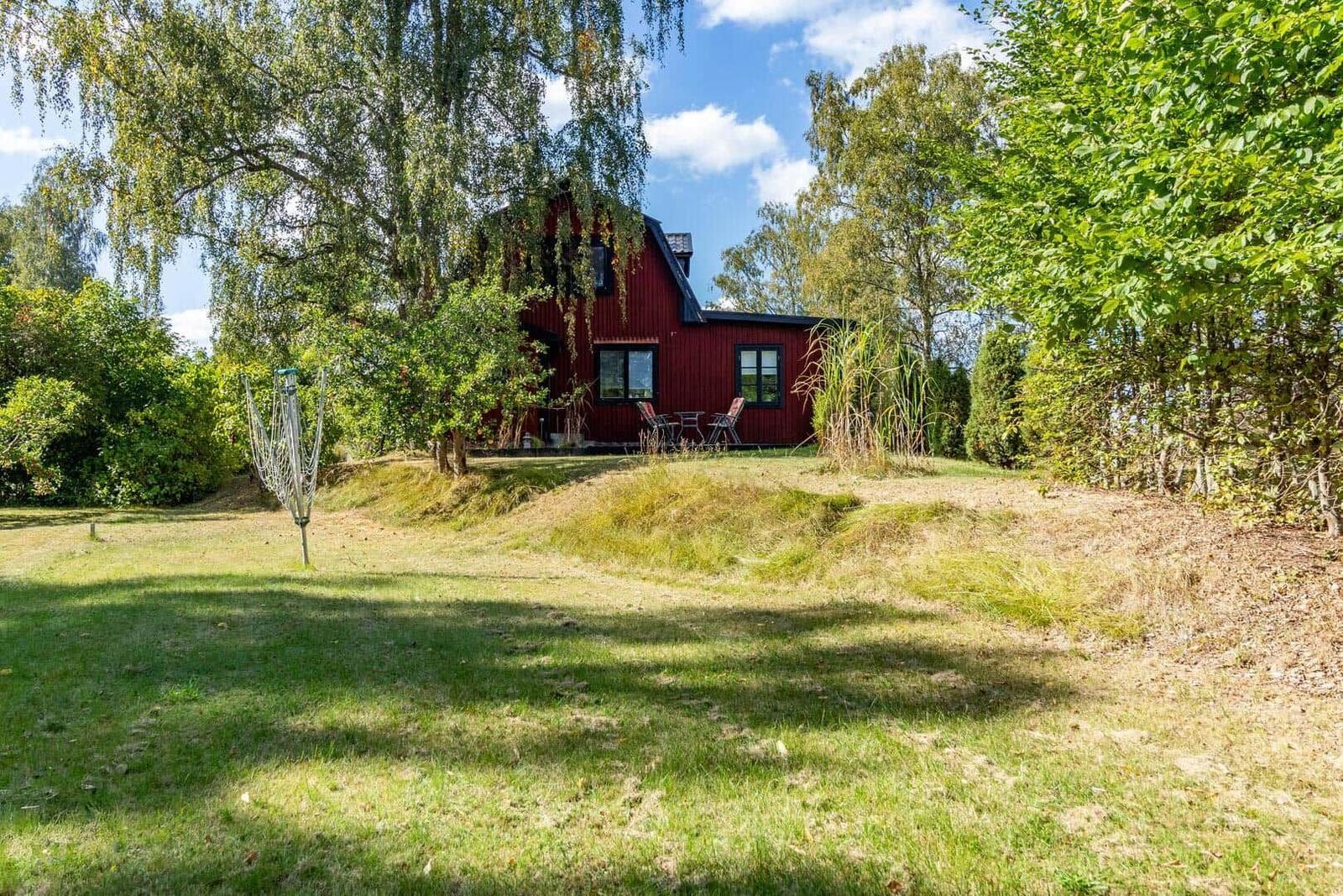Rotes Haus mit Terrasse und Garten unter Bäumen.
