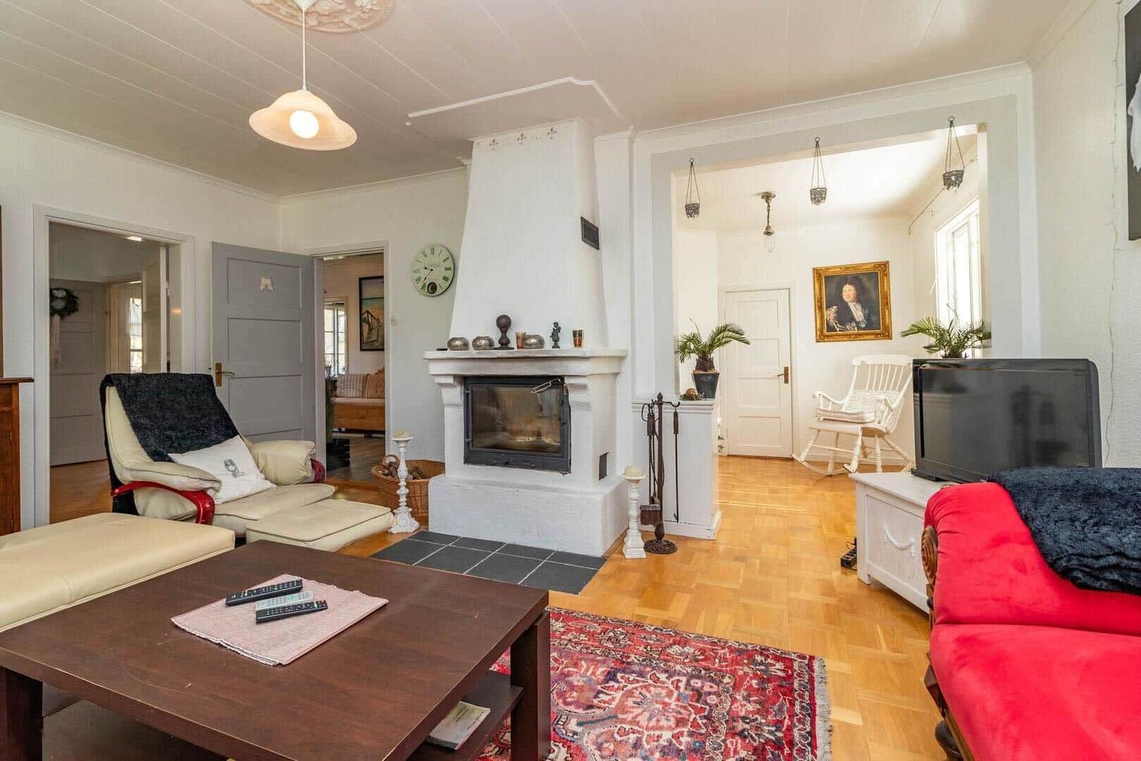 Wohnzimmer mit Kamin, rotem Sofa und Holzboden. Durchgänge zu weiteren Räumen.