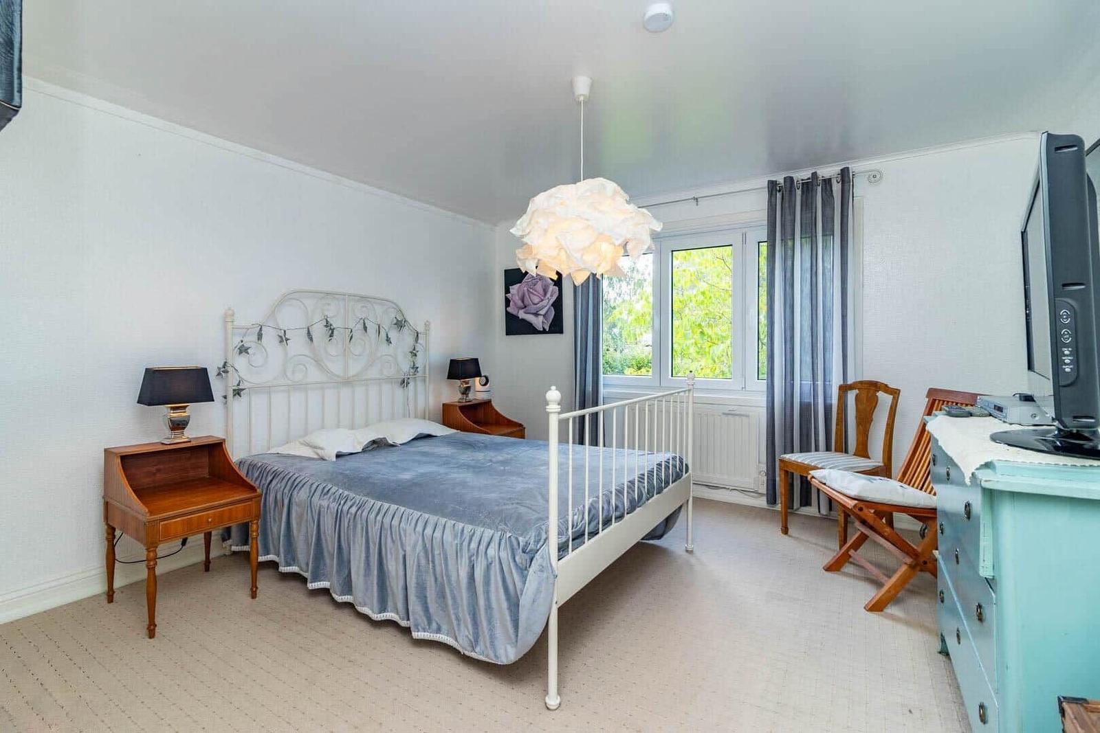 Schlafzimmer mit Bett, Schreibtisch, Fernseher und Fenster mit Blick auf Grün.