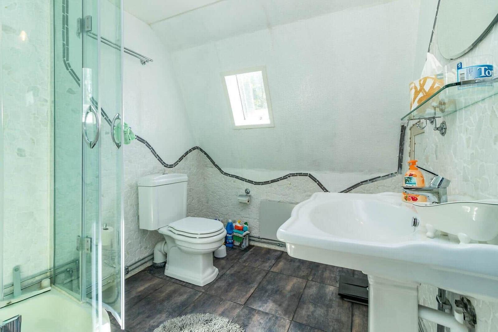 Badezimmer mit Dusche, Toilette und Waschbecken. Wand mit Mosaikverzierung.