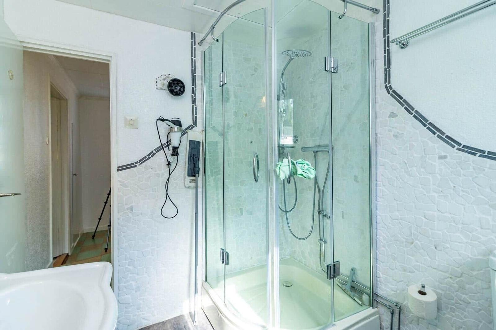 Badezimmer mit Dusche, Toilette und Waschbecken. Wände mit Mosaikfliesen verkleidet.