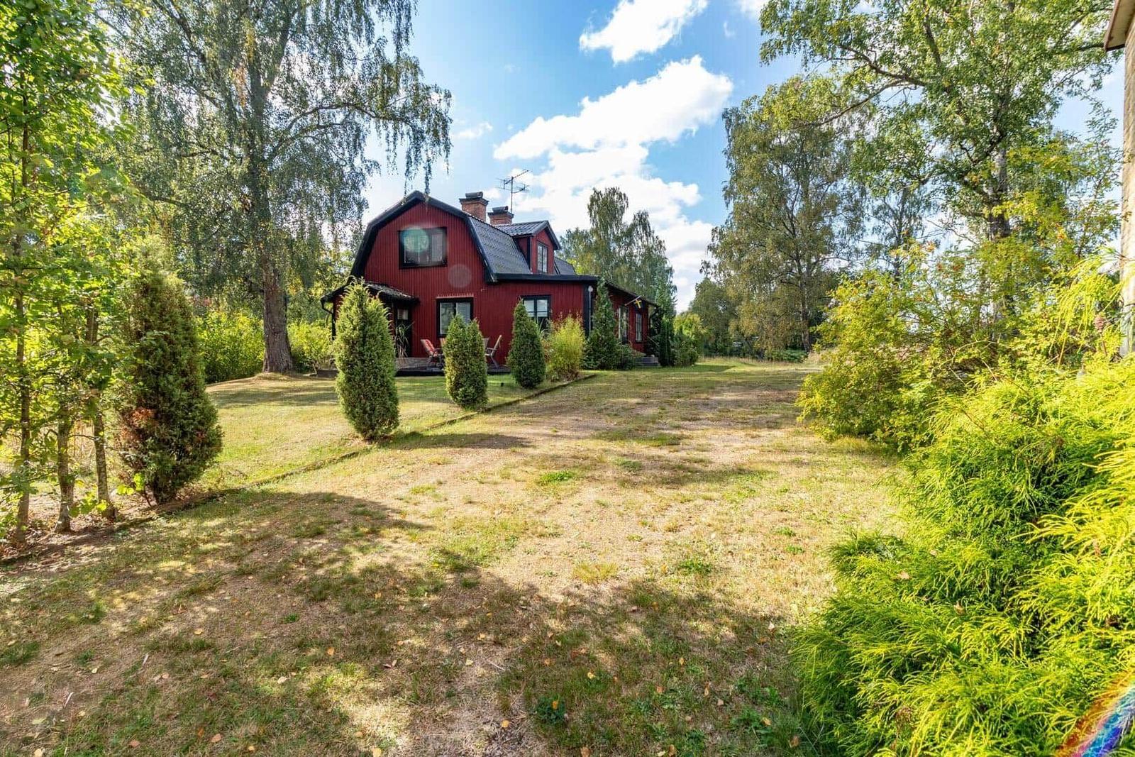 Rotes Haus mit Garten und Bäumen unter blauem Himmel.