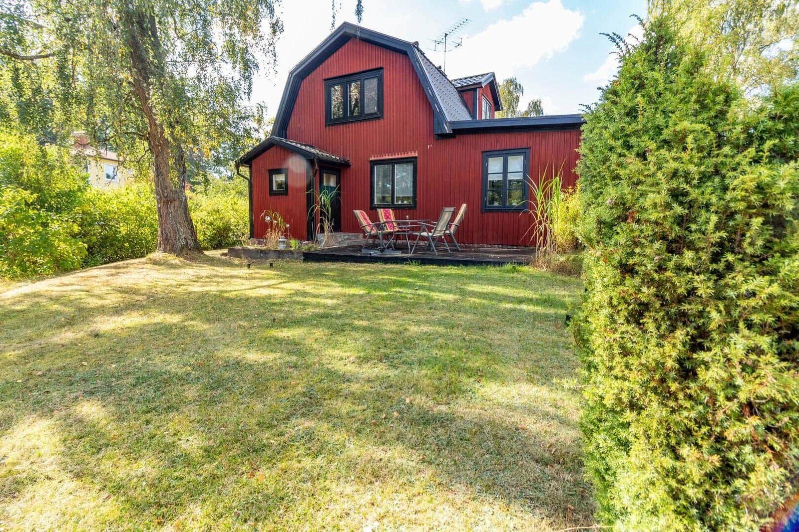 Rotes Holzhaus mit Terrasse und Garten. Möblierte Außenterrasse mit Sitzgelegenheiten.