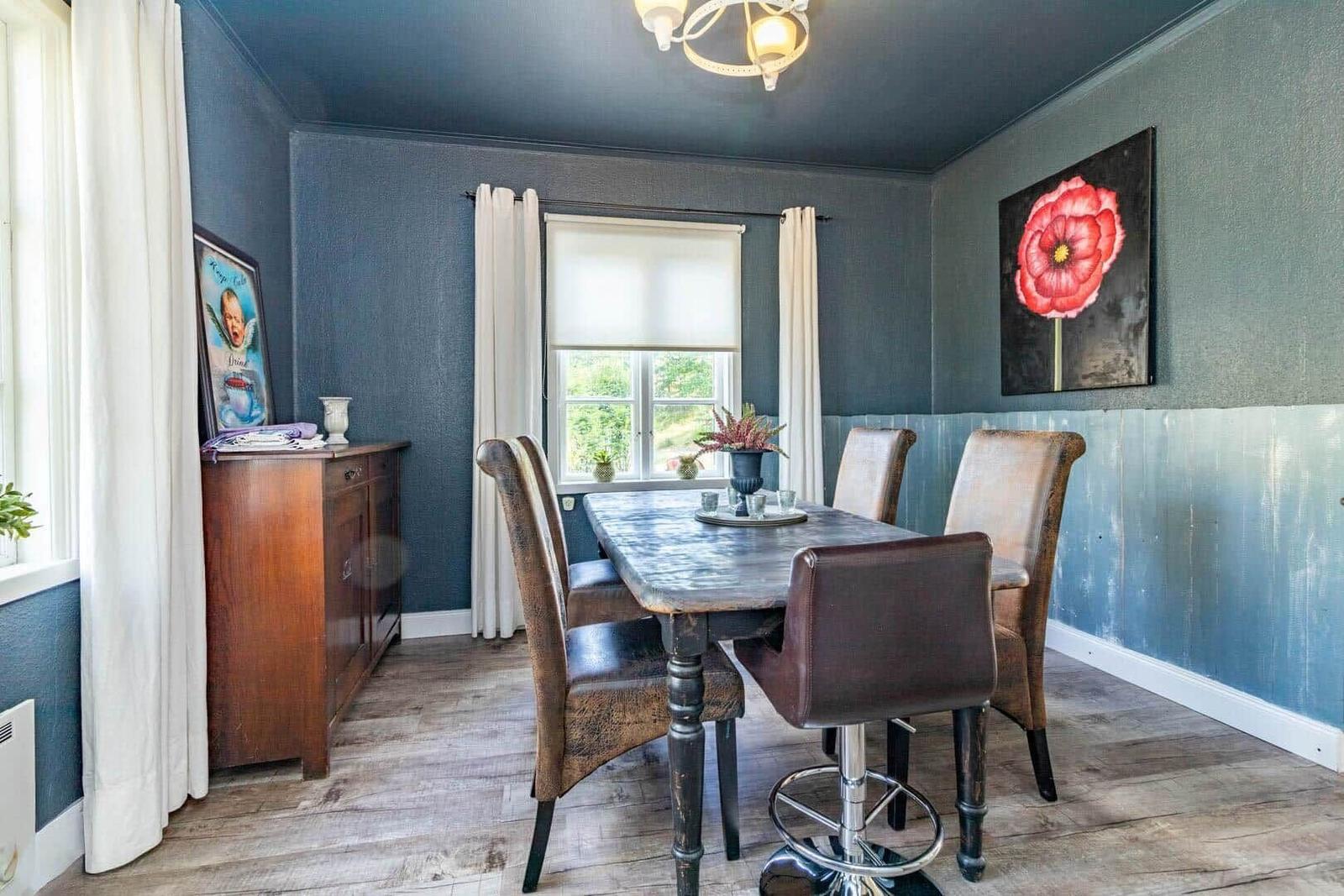 Esszimmer mit Holztisch, Stühlen und Wandbild mit roter Blume.