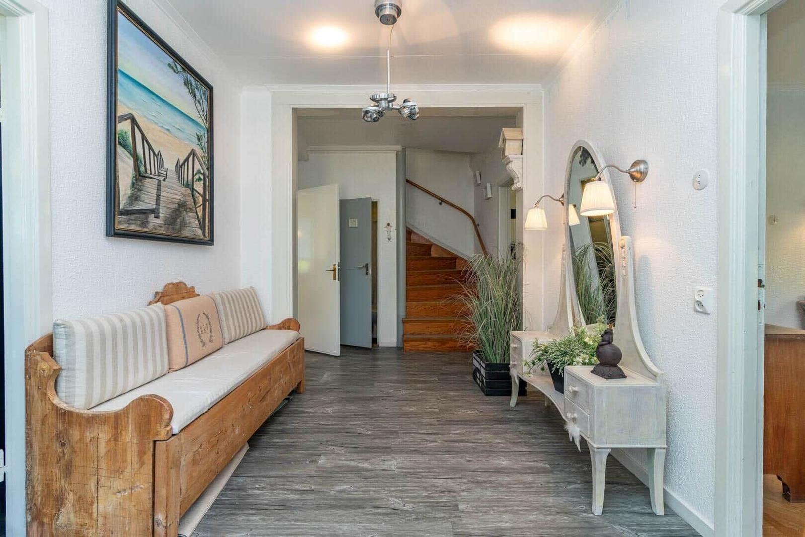 Hausflur mit Holzbank, Spiegel und Treppenaufgang. Wandbild und Pflanzen sichtbar.