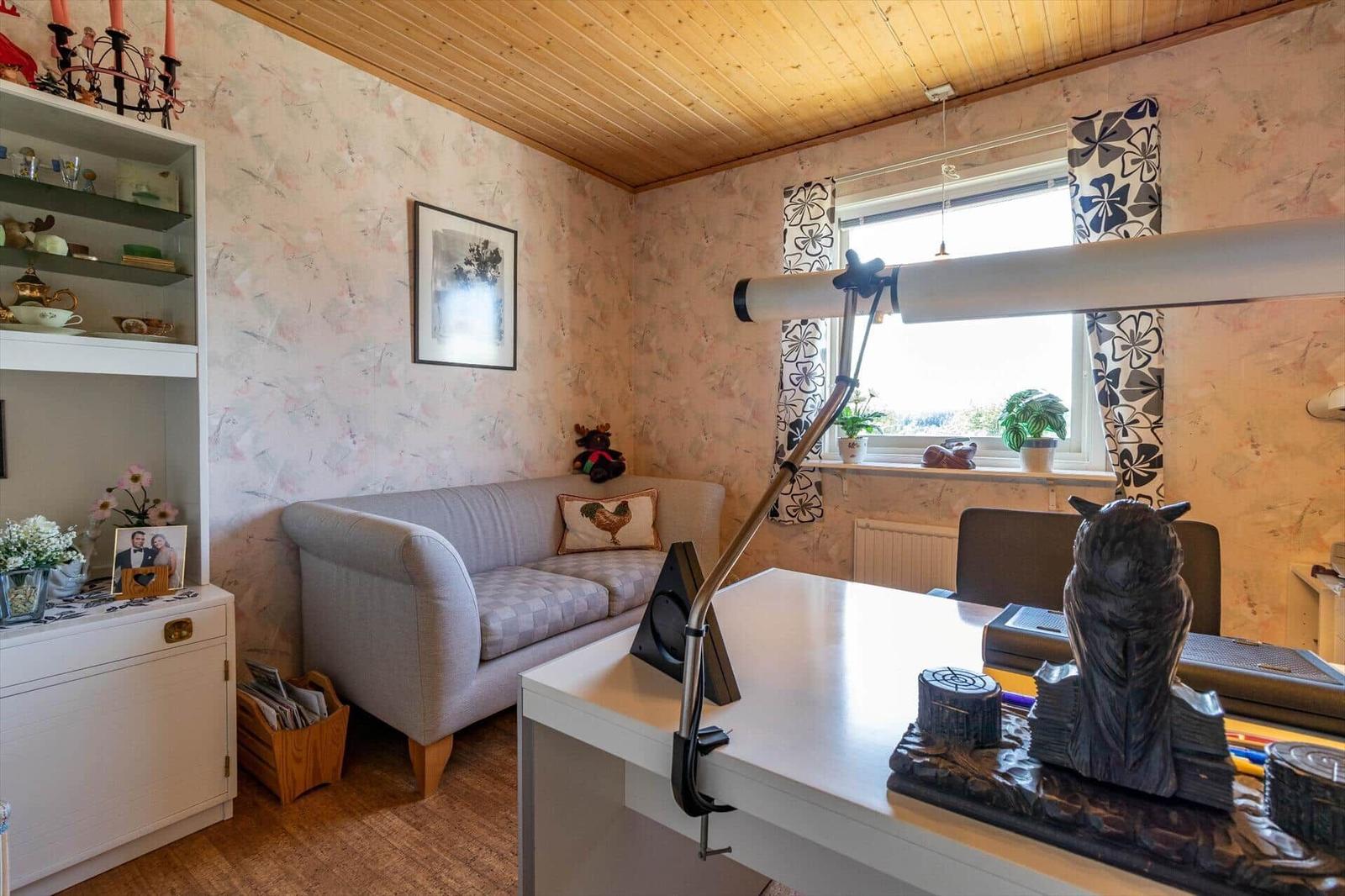 Ein Arbeitszimmer mit Sofa, Schreibtisch und Fenster mit Vorhängen.