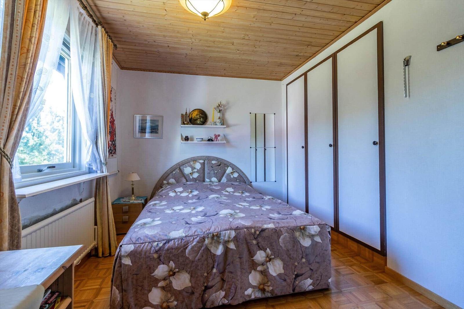 Schlafzimmer mit Bett, Kleiderschrank und Fenster mit Blick auf die Natur.
