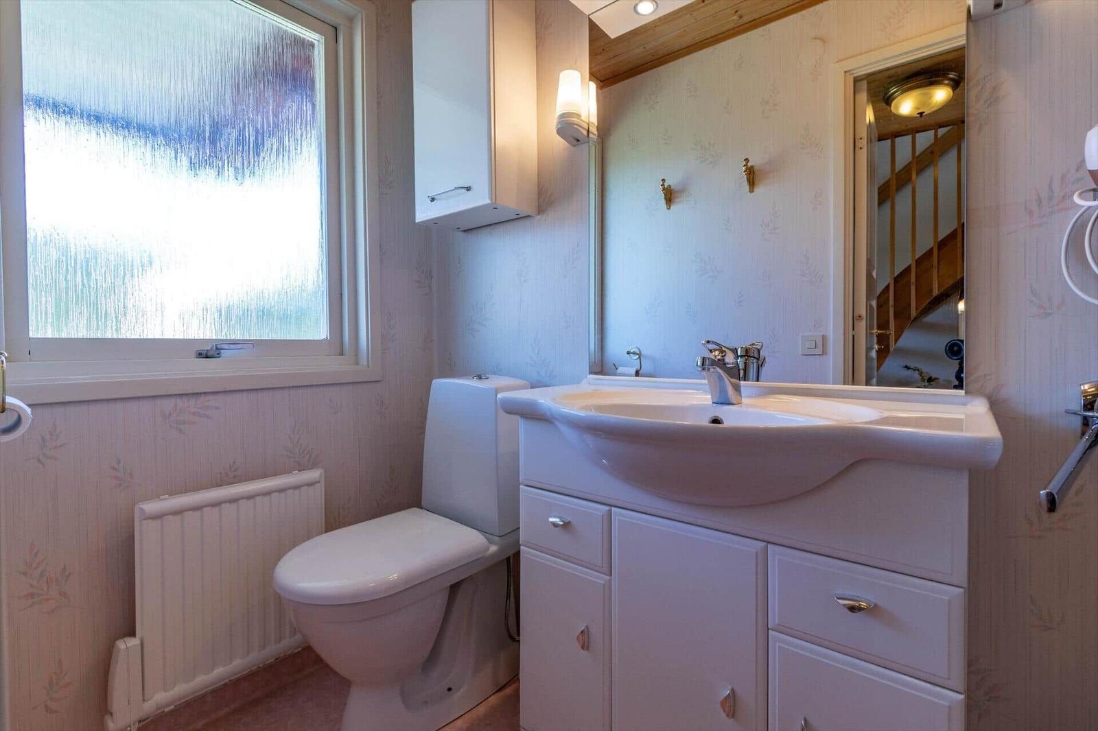 Badezimmer mit Toilette, Waschbecken und Fenster mit getöntem Glas.