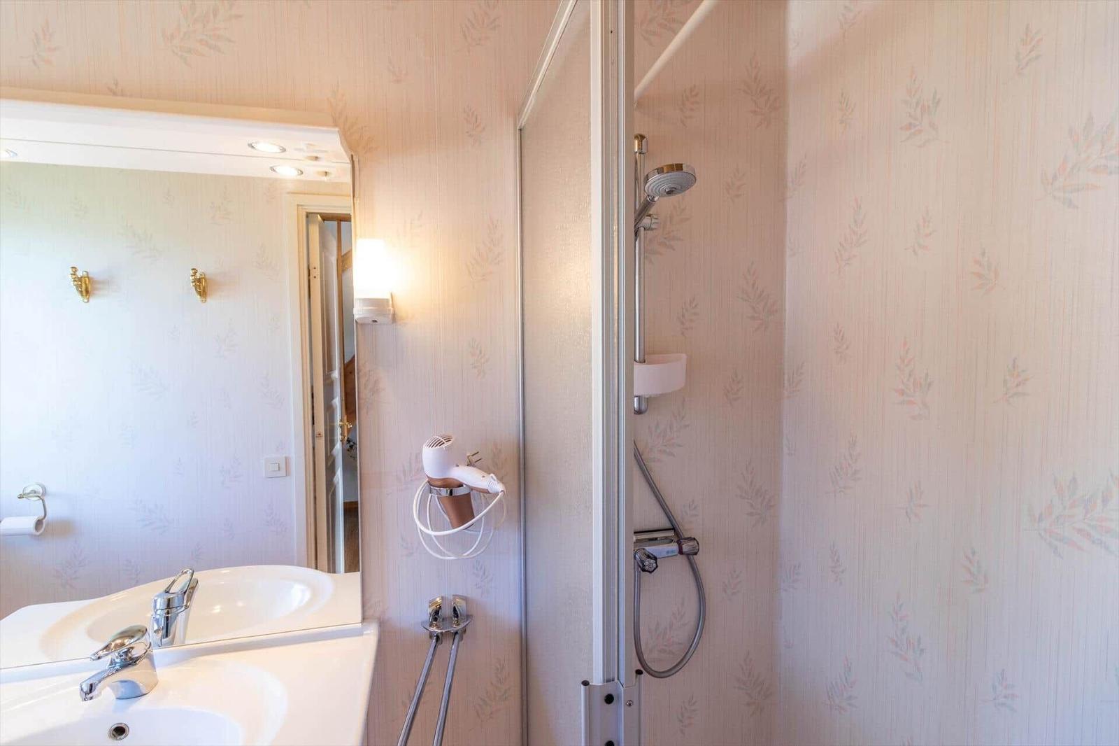 Bad mit Dusche, Waschbecken und Spiegel. Wandverkleidung mit Blattmuster.