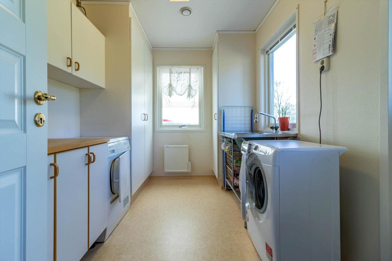 Waschraum mit Waschmaschine, Trockner und Waschbecken. Fenster und Schränke sind vorhanden.