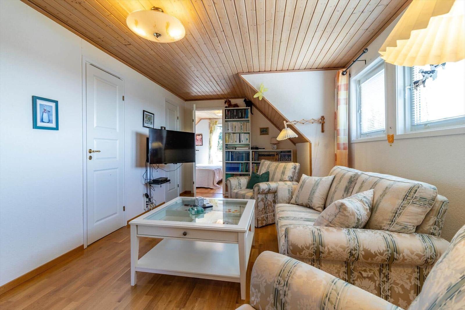 Wohnzimmer mit Sofa, Glas-Tisch, Fernseher und Bücherregal unter Dachschrägen.
