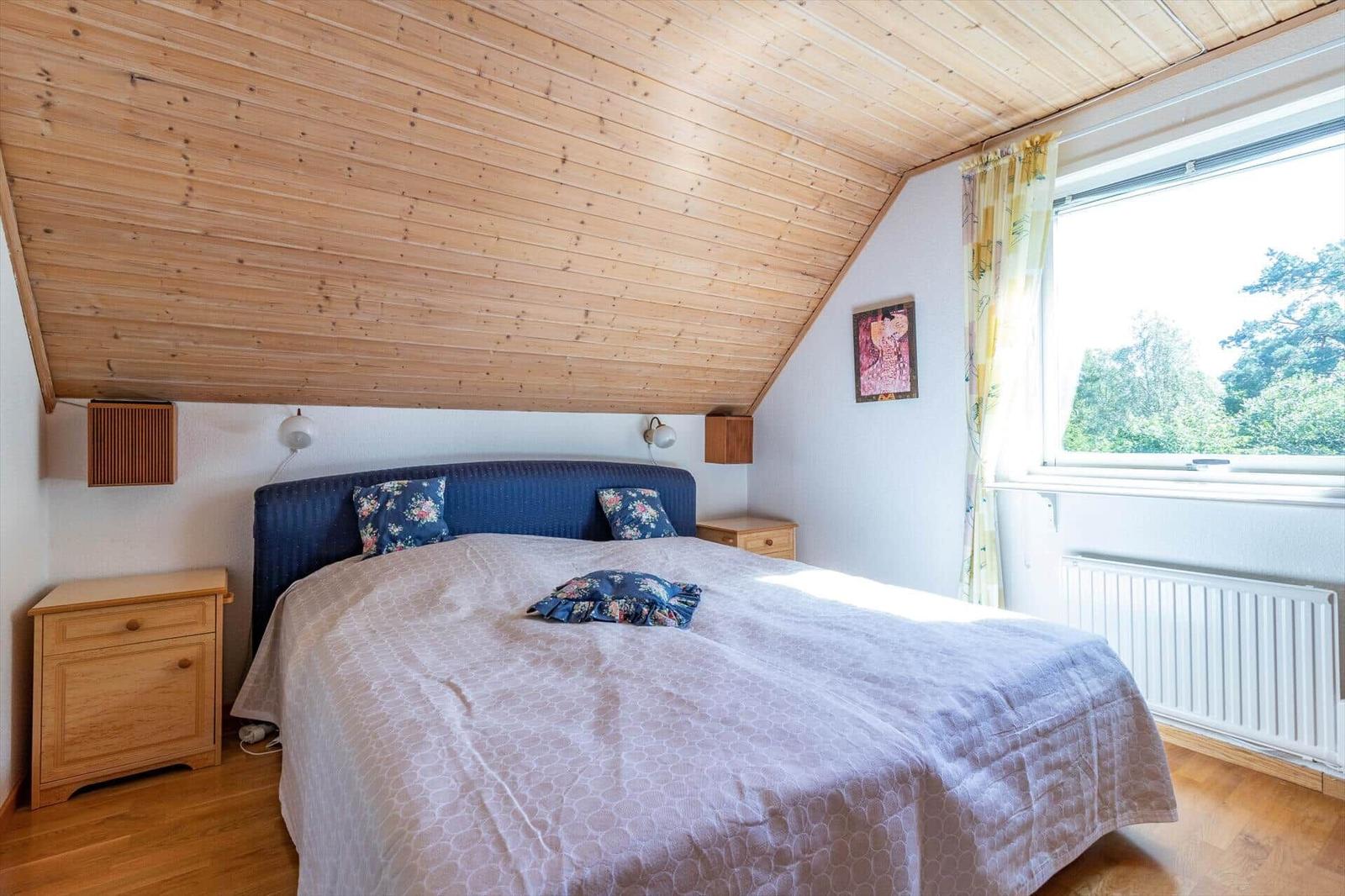 Schlafzimmer mit Holzdecke, Bett und Fenster mit Blick auf Wald.
