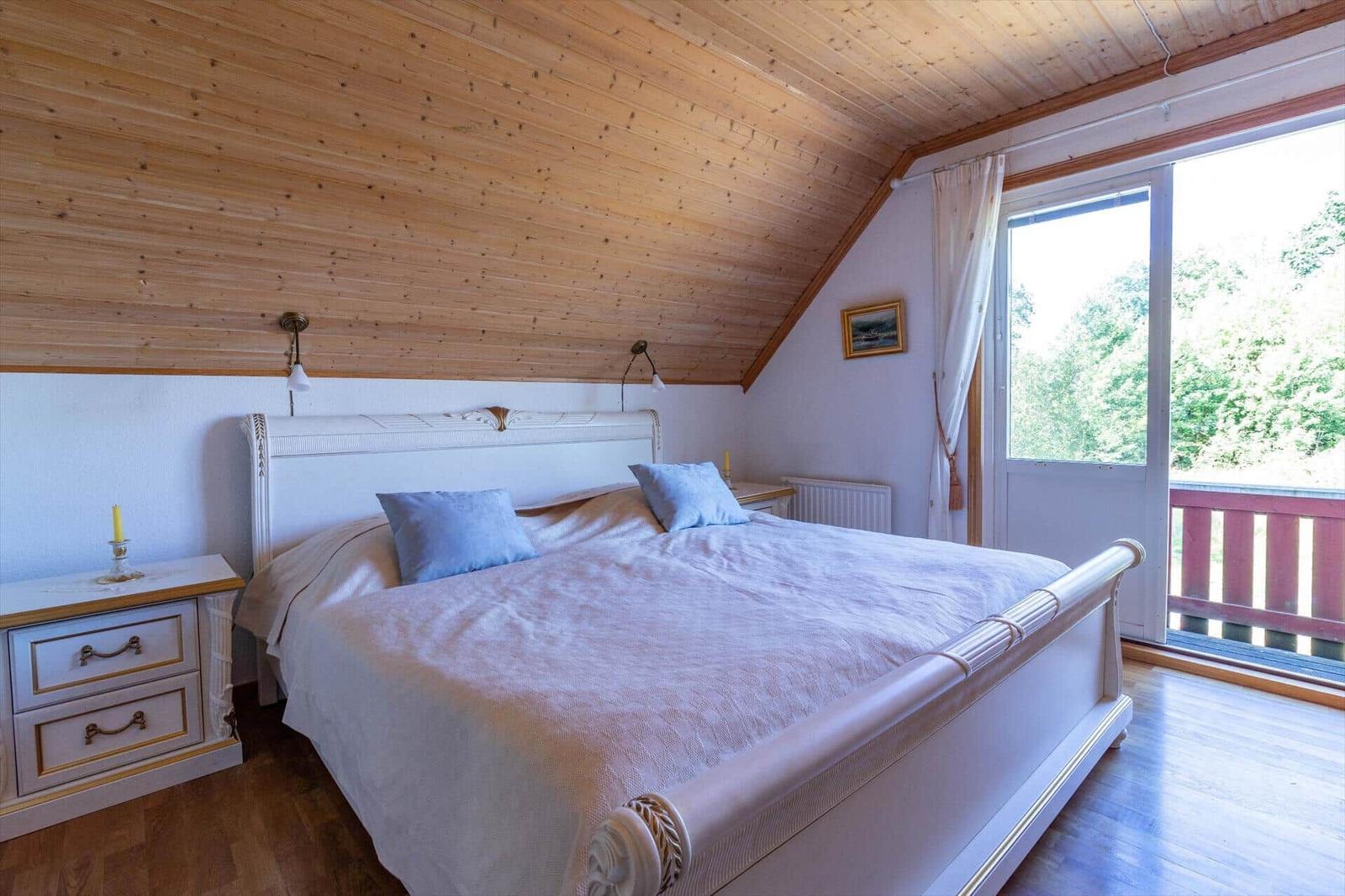 Schlafzimmer mit Doppelbett, Holzdecke und Balkonansicht.