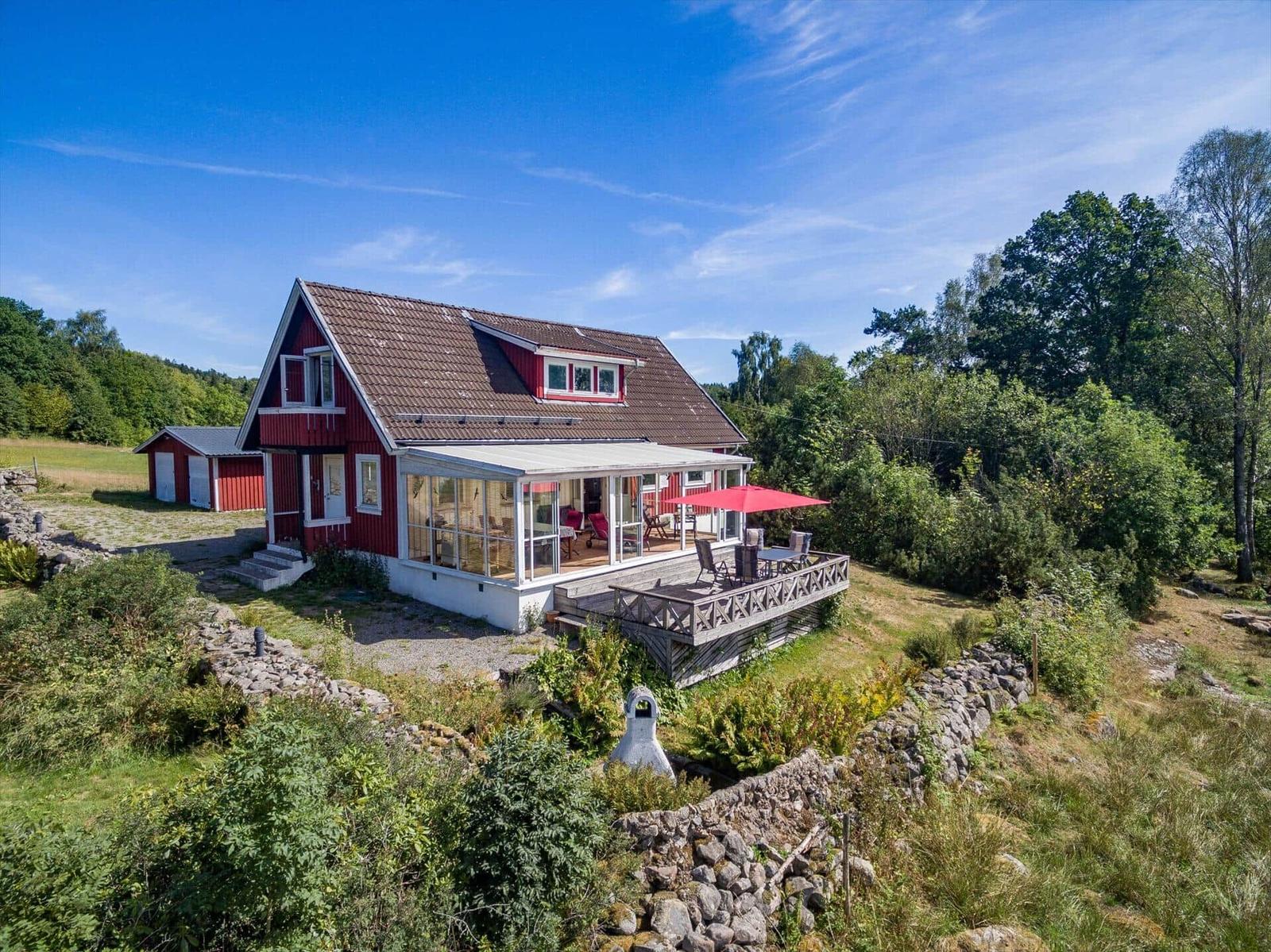 Rotes Haus mit Terrasse und Garten. Roter Sonnenschirm auf der Veranda.