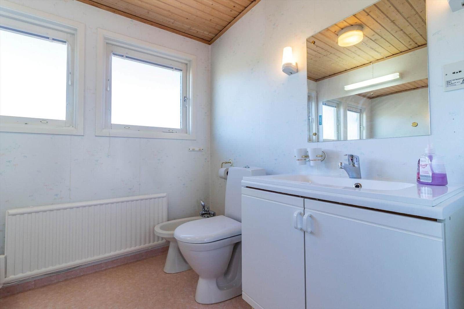 Badezimmer mit Waschbecken, Toilette und Bidet. Holzdecke und zwei Fenster.